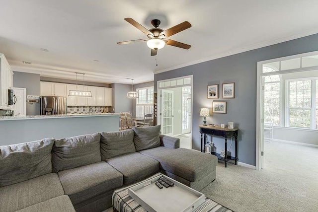 living area with ornamental molding, ceiling fan, baseboards, and light colored carpet
