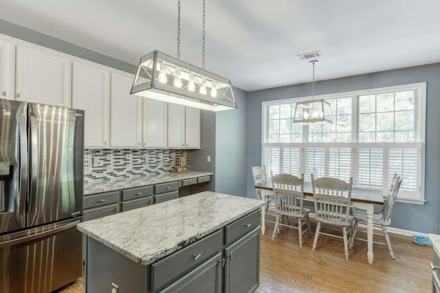 kitchen with decorative backsplash, gray cabinets, stainless steel refrigerator with ice dispenser, visible vents, and a kitchen island