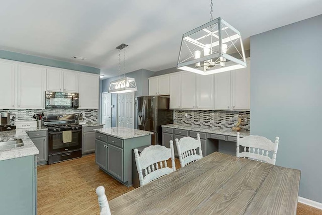 kitchen with an inviting chandelier, a kitchen island, black appliances, and tasteful backsplash