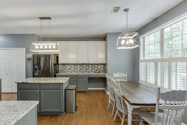 kitchen with wood finished floors, visible vents, gray cabinets, stainless steel fridge, and tasteful backsplash