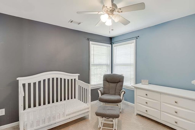 bedroom featuring a ceiling fan, a crib, light carpet, baseboards, and visible vents