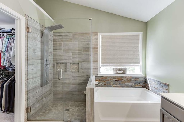 bathroom featuring a stall shower, lofted ceiling, a garden tub, vanity, and a walk in closet