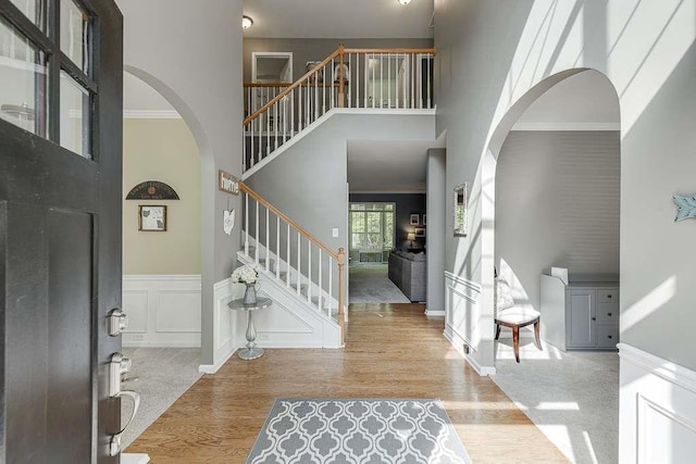 foyer with arched walkways, a high ceiling, wood finished floors, and stairs