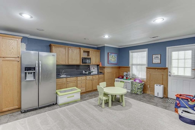 kitchen with crown molding, a sink, wainscoting, black microwave, and stainless steel refrigerator with ice dispenser