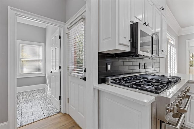 kitchen featuring crown molding, stainless steel appliances, white cabinets, decorative backsplash, and light wood-type flooring