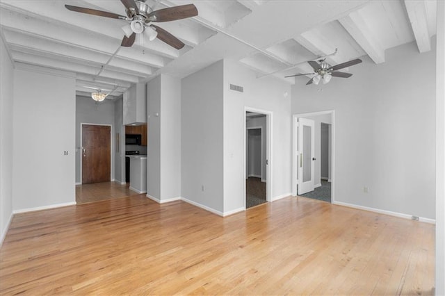 unfurnished room with beam ceiling, light hardwood / wood-style floors, ceiling fan, and a towering ceiling