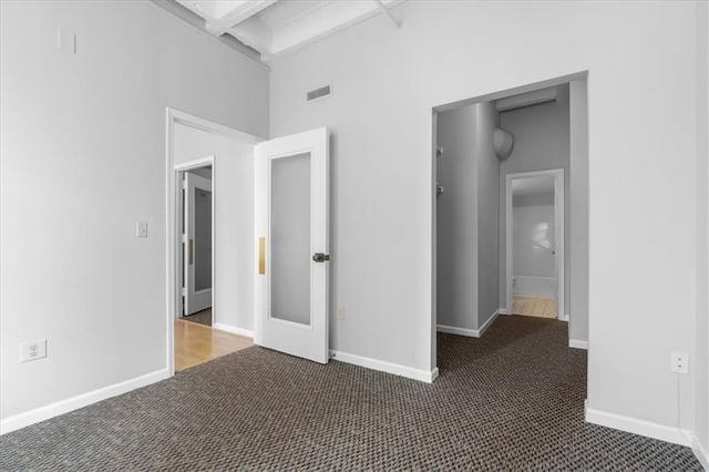 unfurnished bedroom with beam ceiling and dark colored carpet