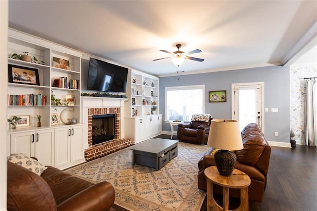 living area featuring wood finished floors, a ceiling fan, baseboards, ornamental molding, and a brick fireplace