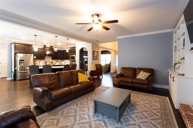 living area featuring arched walkways, dark wood-style flooring, a ceiling fan, baseboards, and ornamental molding