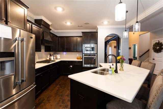 kitchen with arched walkways, custom range hood, appliances with stainless steel finishes, crown molding, and a sink