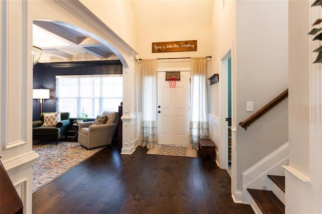 foyer entrance featuring arched walkways, beam ceiling, wood finished floors, coffered ceiling, and stairs