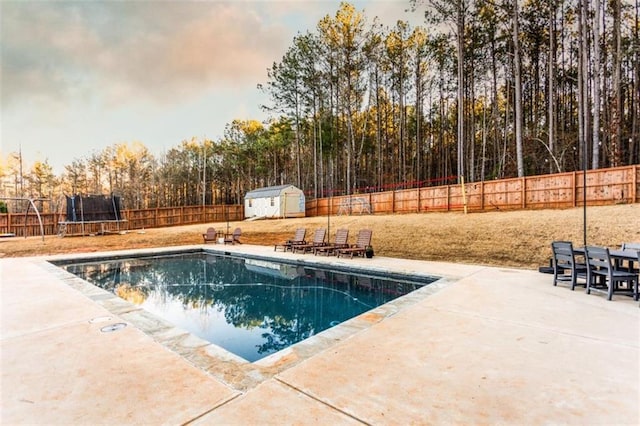 view of swimming pool featuring a fenced backyard, a trampoline, a storage unit, an outdoor structure, and a patio area