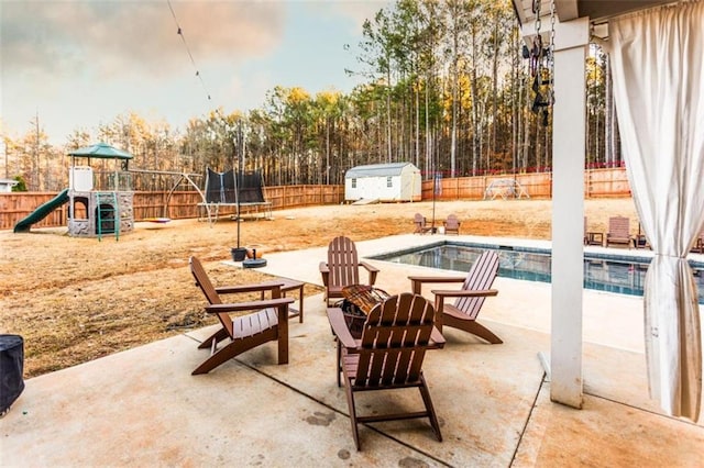 view of patio featuring a storage shed, a fenced backyard, a trampoline, an outdoor structure, and a playground