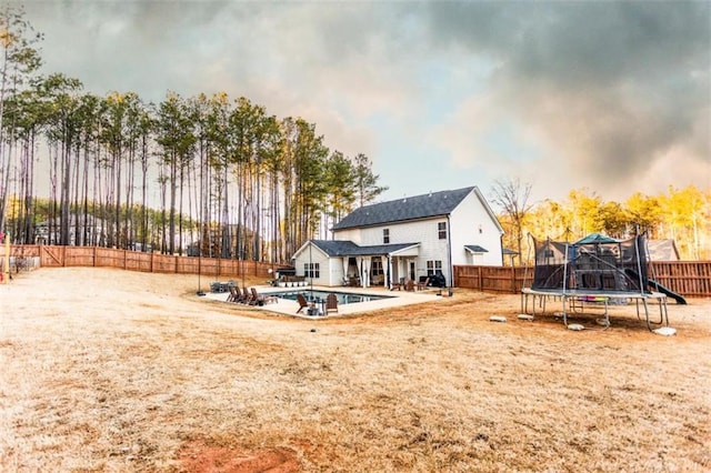 rear view of house with a trampoline, a patio area, a fenced backyard, and a fenced in pool