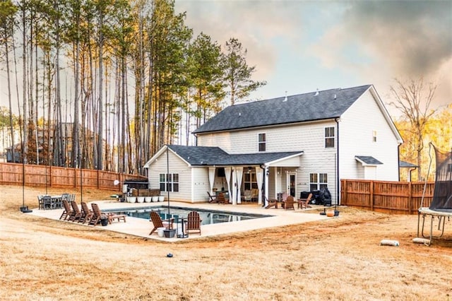 rear view of house with a trampoline, a fenced in pool, a fenced backyard, and a patio