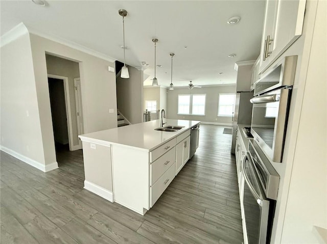 kitchen with appliances with stainless steel finishes, white cabinetry, sink, decorative light fixtures, and an island with sink