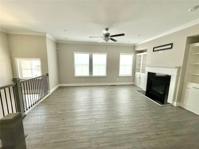 unfurnished living room with built in shelves, hardwood / wood-style floors, and crown molding