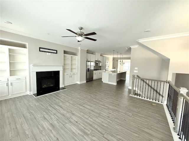 unfurnished living room with crown molding, light hardwood / wood-style floors, and ceiling fan with notable chandelier