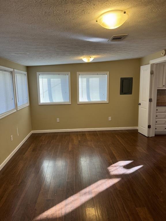 empty room featuring a textured ceiling, a healthy amount of sunlight, and dark hardwood / wood-style floors