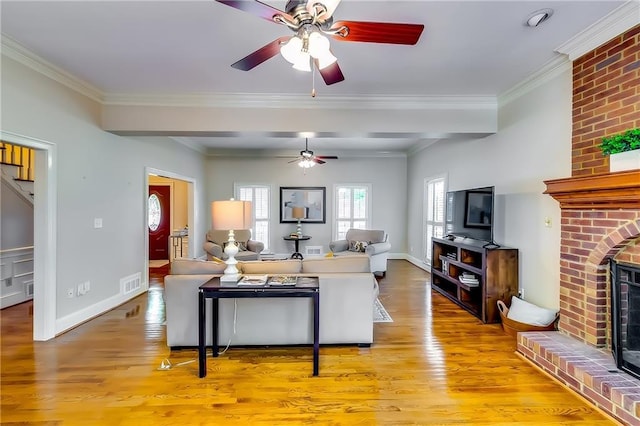 living room with light hardwood / wood-style floors, ornamental molding, ceiling fan, and a brick fireplace