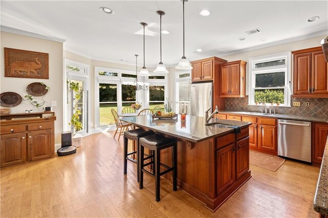 kitchen with appliances with stainless steel finishes, light wood-type flooring, decorative light fixtures, and a kitchen island with sink