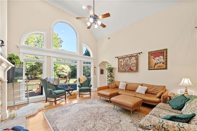 living room with a high end fireplace, ornamental molding, ceiling fan, wood-type flooring, and high vaulted ceiling