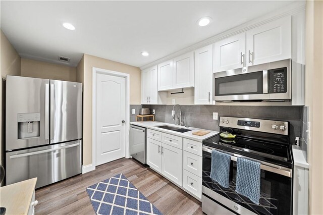 kitchen featuring tasteful backsplash, stainless steel appliances, sink, hardwood / wood-style floors, and white cabinetry