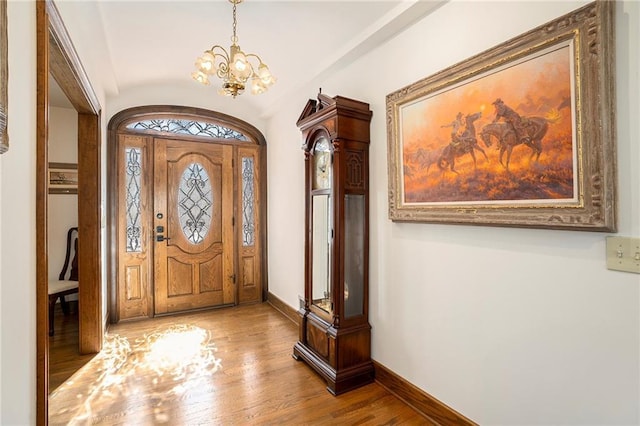 entryway with baseboards, an inviting chandelier, wood finished floors, and vaulted ceiling