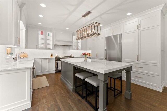 kitchen with high end appliances, a sink, a breakfast bar area, a center island, and white cabinetry