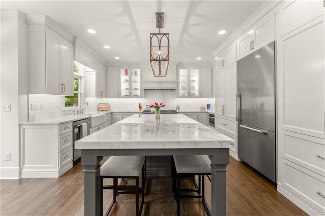 kitchen featuring stainless steel appliances, backsplash, light stone countertops, dark wood-type flooring, and recessed lighting