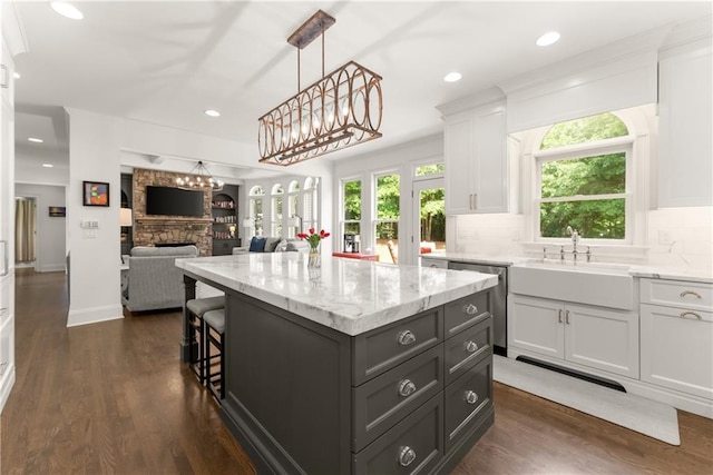 kitchen with a sink, white cabinetry, stainless steel dishwasher, a kitchen island, and dark wood-style floors