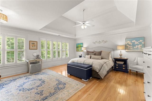 bedroom with light wood-style floors, a raised ceiling, baseboards, and a ceiling fan