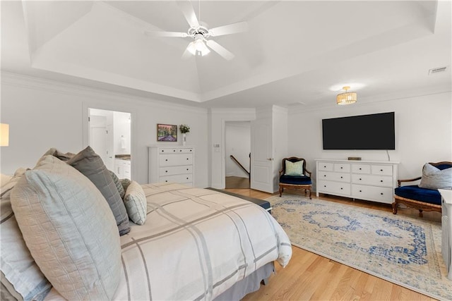 bedroom featuring a tray ceiling, wood finished floors, ensuite bath, and ceiling fan