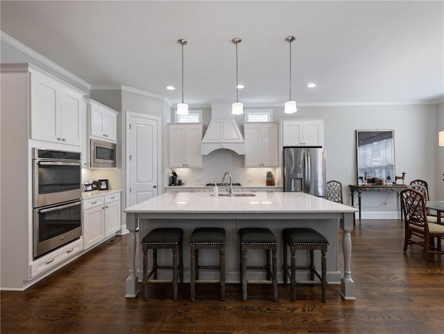 kitchen featuring appliances with stainless steel finishes, decorative light fixtures, an island with sink, and white cabinets