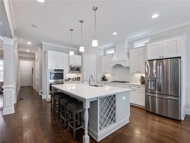 kitchen with pendant lighting, premium range hood, appliances with stainless steel finishes, decorative columns, and white cabinets