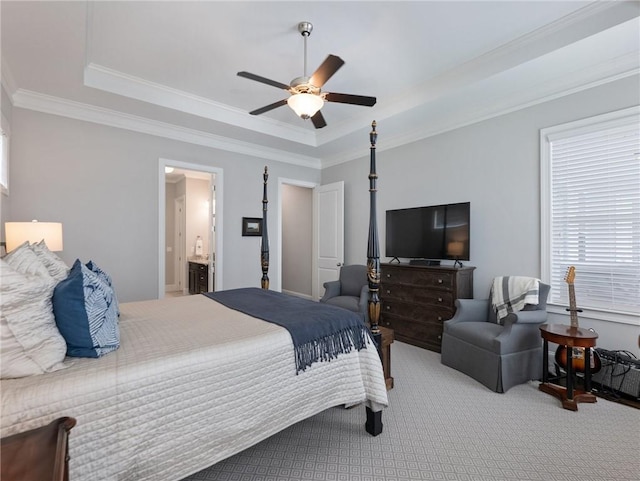 carpeted bedroom with ornamental molding, ensuite bath, ceiling fan, and a tray ceiling