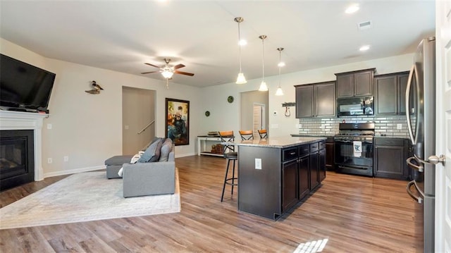 kitchen with a kitchen bar, light stone counters, decorative light fixtures, a kitchen island, and black appliances