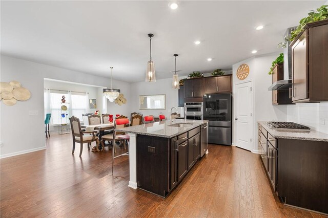 kitchen featuring a kitchen bar, sink, light stone counters, hanging light fixtures, and an island with sink