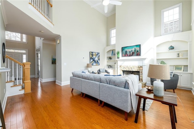 living room featuring built in shelves, a stone fireplace, crown molding, wood-type flooring, and a towering ceiling