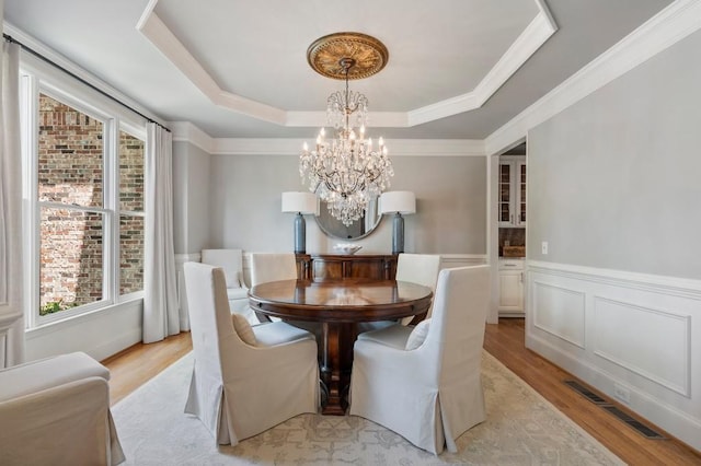 4250 Old Oak Trce, Cumming, GA 30041 - dining space with a chandelier, light wood-style floors, a raised ceiling, a wainscoted wall, and ornamental molding