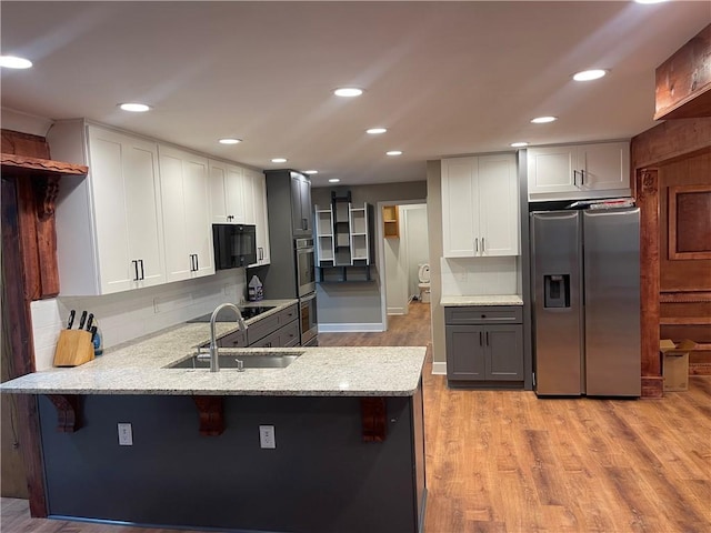 1321 Earle Ct SE, Conyers, GA 30013 - kitchen with black appliances, a sink, a peninsula, light stone counters, and light wood-type flooring