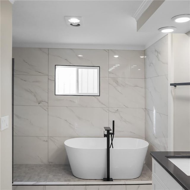 bathroom with a freestanding bath, crown molding, vanity, and tile walls