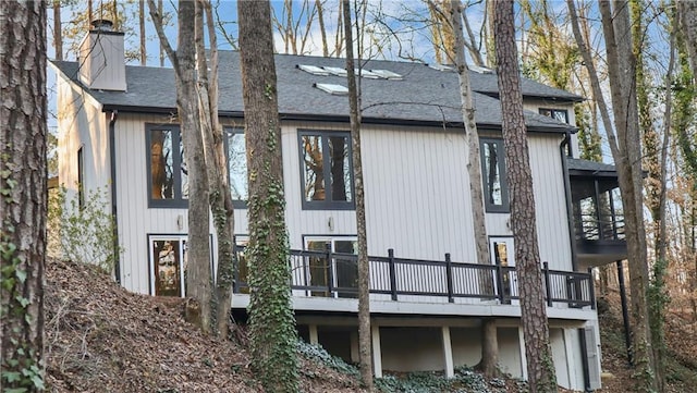 rear view of property with a shingled roof, a chimney, and a wooden deck