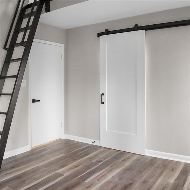 spare room featuring a barn door, wood finished floors, and baseboards