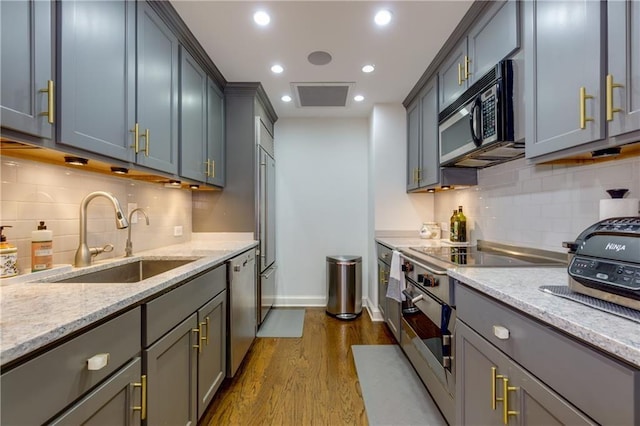 kitchen with light stone countertops, stainless steel dishwasher, dark wood-type flooring, and a sink