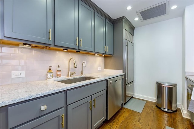 kitchen featuring sink, appliances with stainless steel finishes, backsplash, dark hardwood / wood-style floors, and light stone counters