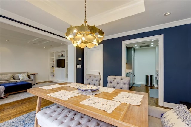 dining area featuring wood-type flooring, ornamental molding, built in features, and an inviting chandelier