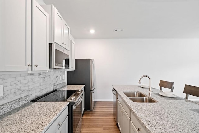 kitchen with sink, a breakfast bar area, appliances with stainless steel finishes, white cabinetry, and light stone counters