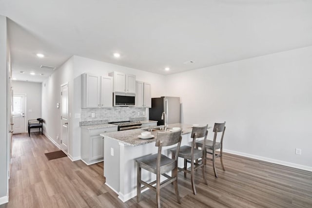 kitchen with tasteful backsplash, an island with sink, a breakfast bar area, stainless steel appliances, and light stone countertops