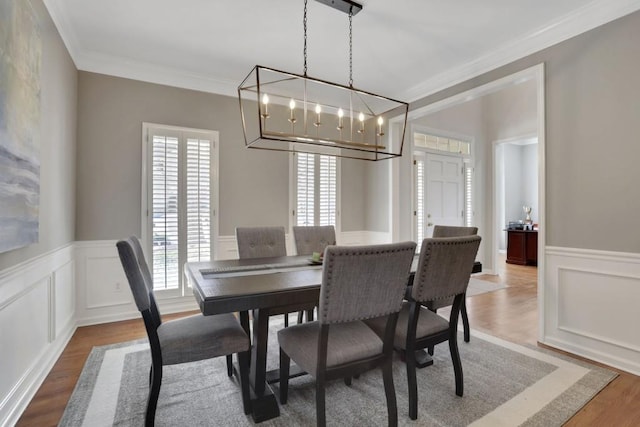 dining space with ornamental molding, a decorative wall, wood finished floors, and wainscoting